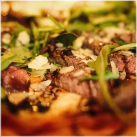 Pizza met dun gesneden ossenhaas, mozzarella, pesto, rucola, balsamico creme en Parmezaanse kaas